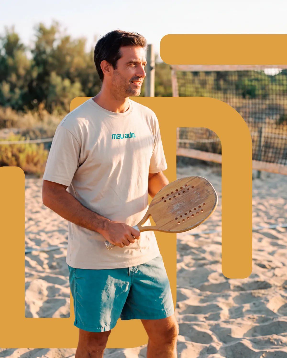 Professor de beach tênis com a raquete na mão em uma quadra de areia, vestindo camiseta do MeuADM